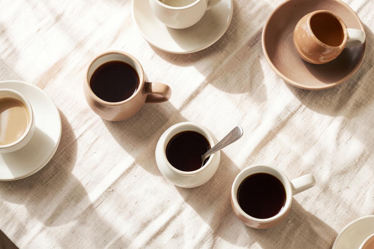 Several coffee cups arranged on a cream linen tablecloth photographed from above in window light